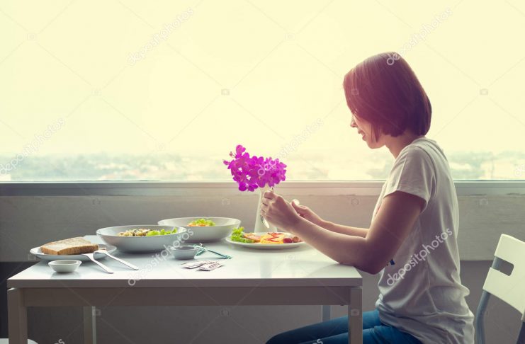 Young woman sitting at a room on table and eating dinner alone.