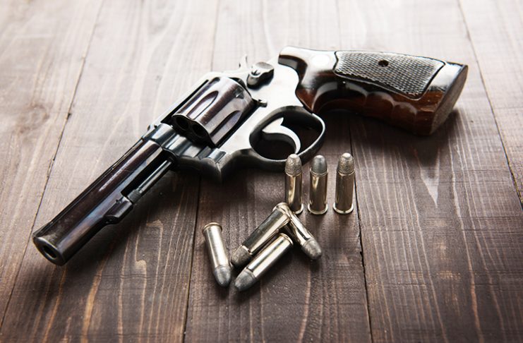 black revolver gun with bullets isolated on wooden background.