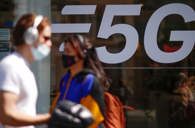 People, wearing protective face masks, walk past a 5G data network sign at a mobile phone store in Paris, France, April 22, 2021. REUTERS/Gonzalo Fuentes